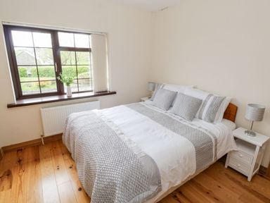 A bedroom with a double bed with grey and white bedding beside a window with a vase and radiator at Doonalton House in Dromore West County Sligo