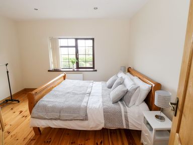 A bedroom with a wooden bed frame and gray bedding next to a white nightstand with a lamp at Doonalton House in Dromore West County Sligo