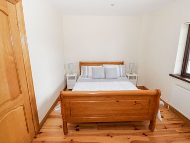 A bedroom with a wooden bed frame white bedding two white nightstands with lamps and a window at Doonalton House in Dromore West County Sligo