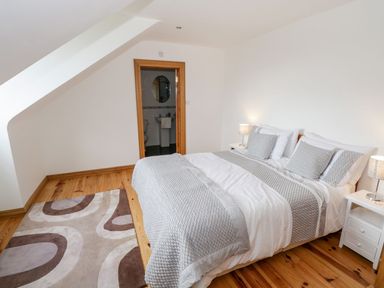 A bedroom with a double bed covered with white and gray bedding two bedside tables with lamps and a view into a bathroom at Doonalton House in Dromore West County Sligo