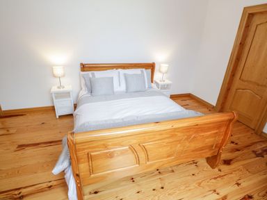 A bedroom with a wooden bed frame white bedding two white bedside tables with lamps and a wooden door at Doonalton House in Dromore West County Sligo