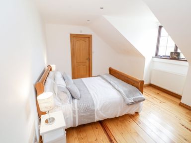 A bedroom with a wooden bed white and gray bedding a wooden door a window with a radiator and a bedside table with a lamp at Doonalton House in Dromore West County Sligo