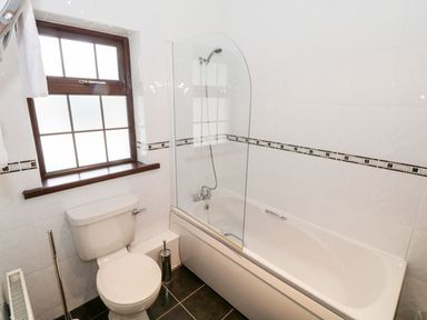 A bathroom with a toilet next to a bathtub with a shower screen and window at Doonalton House in Dromore West County Sligo