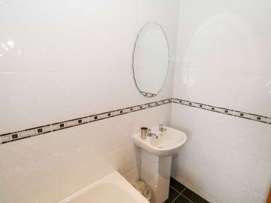 A bathroom corner with a small pedestal sink, oval mirror, tiled walls with decorative border and a bathtub at Doonalton House in Dromore West County Sligo