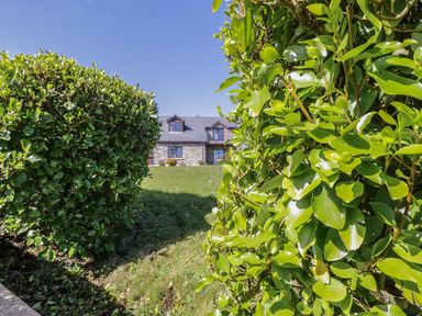 A stone house with dormer windows behind green bushes and a grassy area at Doonalton House in Dromore West County Sligo