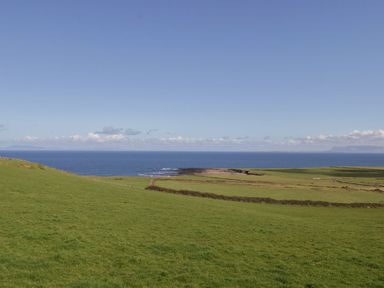 A view of green fields leading to the sea under a clear blue sky at Doonalton House in Dromore West County Sligo