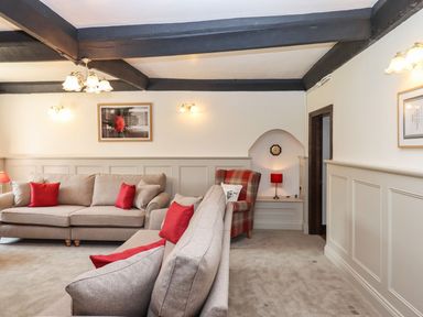 A living room with beige sofas and red cushions and a plaid armchair with a red lamp at Nempnett Farmhouse Nempnett Thrubwell near Blagdon