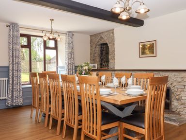 A dining room with a wooden table set for twelve near a stone wall at Nempnett Farmhouse in Nempnett Thrubwell near Blagdon