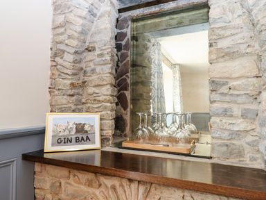 A wooden shelf with wine glasses on a tray and a framed picture leaning on a stone wall at Nempnett Farmhouse in Nempnett Thrubwell near Blagdon