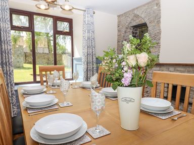 A dining room with a wooden table set with white plates and floral napkins by a window at Nempnett Farmhouse in Nempnett Thrubwell near Blagdon