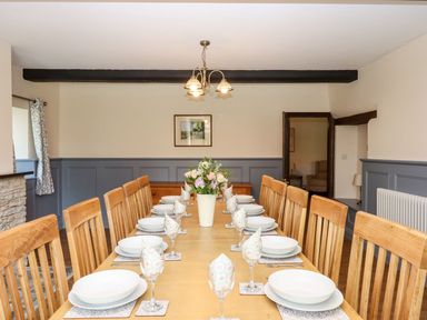 A dining room with a long wooden table set with plates glasses and napkins with wooden chairs and gray paneled walls at Nempnett Farmhouse Nempnett Thrubwell near Blagdon