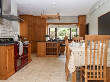 A kitchen with wooden cabinets red stove dining table with chairs and a window at Nempnett Farmhouse in Nempnett Thrubwell near Blagdon