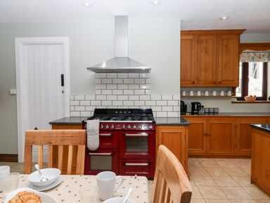A kitchen with a red stove and wooden cabinets and a table set for breakfast at Nempnett Farmhouse in Nempnett Thrubwell near Blagdon