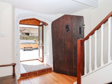 A hallway with a wooden door open to an outdoor area with a hot tub and a wooden staircase with white balusters inside Nempnett Farmhouse in Nempnett Thrubwell near Blagdon