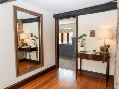 A hallway with wooden floor a wall mirror and a wooden table with lamp plant and books at Nempnett Farmhouse Nempnett Thrubwell near Blagdon