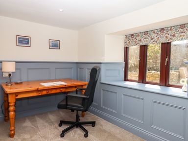 A study with a wooden desk black office chair table lamp and floral roman blinds on the windows at Nempnett Farmhouse Nempnett Thrubwell near Blagdon