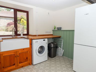 A laundry room with a washing machine sink wooden cabinets trash bin and refrigerator at Nempnett Farmhouse Nempnett Thrubwell near Blagdon