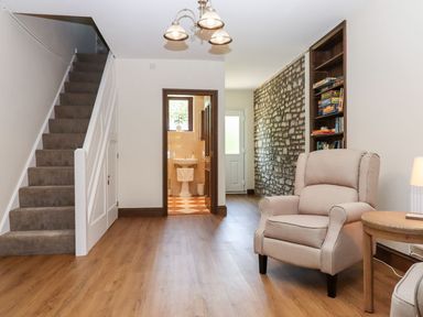 A room with carpeted stairs a wooden floor a beige armchair a wooden side table a stone wall with built-in shelves and a bathroom visible through a doorway at Nempnett Farmhouse in Nempnett Thrubwell near Blagdon