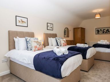 A bedroom with three single beds each with pillows, blankets, rolled towels, animal-themed artwork on walls and wooden furniture at Nempnett Farmhouse in Nempnett Thrubwell near Blagdon
