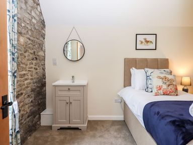 A bedroom with a bed featuring animal-themed pillows a bedside lamp and a sink with a round mirror on the wall at Nempnett Farmhouse in Nempnett Thrubwell near Blagdon