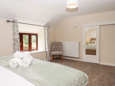 A bedroom with rolled towels on a bed a chair near a window and a mirror on a sliding door at Nempnett Farmhouse in Nempnett Thrubwell near Blagdon