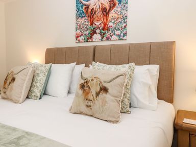 A bed with animal and floral cushions a beige headboard and a wooden bedside table at Nempnett Farmhouse Nempnett Thrubwell near Blagdon