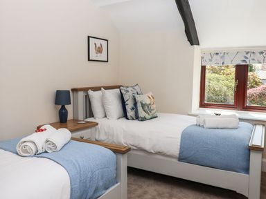 A bedroom with two single beds white bedding blue throws and pillows a bedside table with lamp and a window at Nempnett Farmhouse in Nempnett Thrubwell near Blagdon