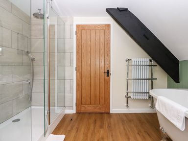 A bathroom with a glass shower enclosure wooden door towel radiator and clawfoot bathtub at Nempnett Farmhouse in Nempnett Thrubwell near Blagdon
