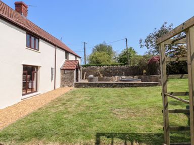 A backyard with grass a patio area with outdoor seating and a round table a side of a house with windows and a gravel path at Nempnett Farmhouse Nempnett Thrubwell near Blagdon