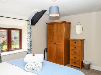 A bedroom with a wooden wardrobe and chest of drawers next to a window with floral curtains at Nempnett Farmhouse in Nempnett Thrubwell near Blagdon