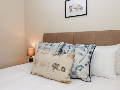 A bed with pillows featuring floral and animal prints with a lamp and pig artwork at Nempnett Farmhouse in Nempnett Thrubwell near Blagdon