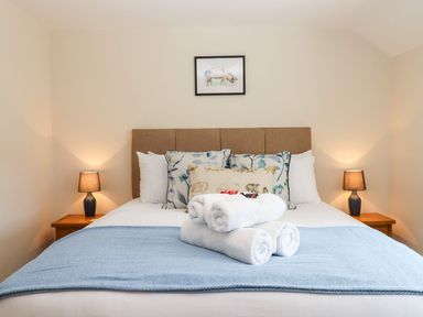 A bed with rolled white towels on blue blanket and floral pillows with lamps on wooden side tables at Nempnett Farmhouse in Nempnett Thrubwell near Blagdon
