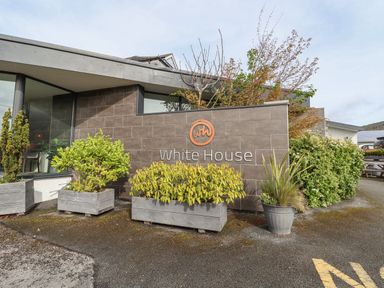A building with a brown tiled wall displaying the sign white house surrounded by plants in wooden and plastic pots at Lodge 3 in St Asaph