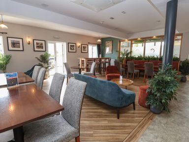 A dining area with tables chairs sofas and plants at Lodge 3 in St Asaph