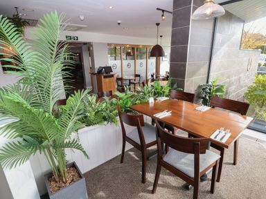 A dining area with wooden tables and chairs surrounded by plants at Lodge 3 in St Asaph