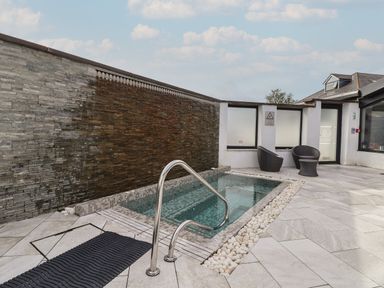 An outdoor hot tub with tiled walls a metal handrail and two chairs with a small table at Lodge 3 in St Asaph
