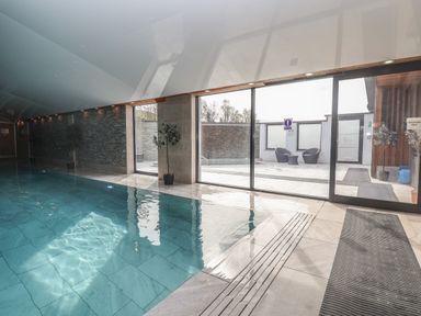 An indoor swimming pool with tiled floor and glass doors leading to an outdoor seating area at Lodge 3 in St Asaph