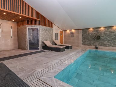 An indoor pool with two lounge chairs next to a tiled wall and a door at Lodge 3 in St Asaph