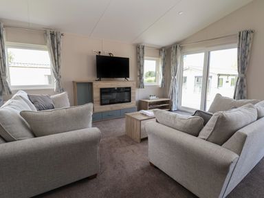 A living room with two sofas a TV on a stand a coffee table and windows with curtains at Lodge 3 in St Asaph