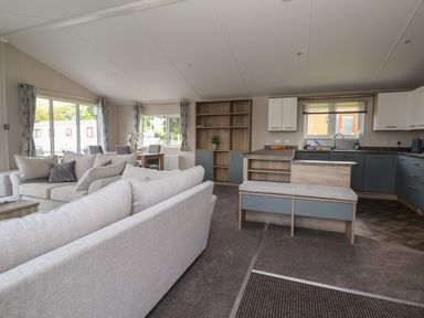 An open-plan living room and kitchen with sofas a dining table and chairs shelving unit and kitchen cabinets at Lodge 3 in St Asaph