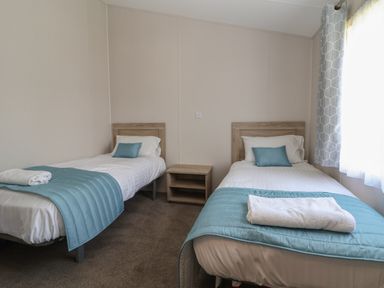 A bedroom with two single beds a nightstand and a window with curtains at Lodge 3 in St Asaph