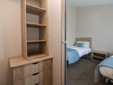 A bedroom with two single beds a bedside table and a wooden chest of drawers with shelves at Lodge 3 in St Asaph
