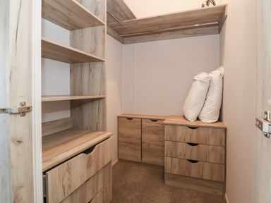 A walk-in closet with wooden shelves drawers and two white pillows on a drawer at Lodge 3 in St Asaph