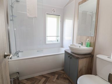 A bathroom with a bathtub shower combo a window a sink with a mirror and a toilet at Lodge 3 in St Asaph