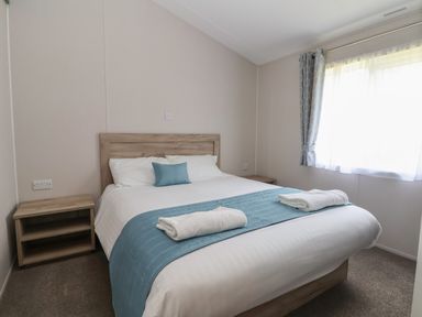 A bedroom with a double bed two bedside tables a window with curtains and towels on the bed at Lodge 3 in St Asaph