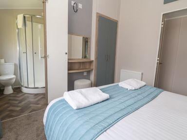 A bedroom with a bed and two towels with an attached bathroom with a shower and toilet at Lodge 3 in St Asaph