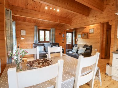 A wooden cabin interior with a dining table and white chairs and leather sofas at Kingfisher Lodge in Badwell Ash