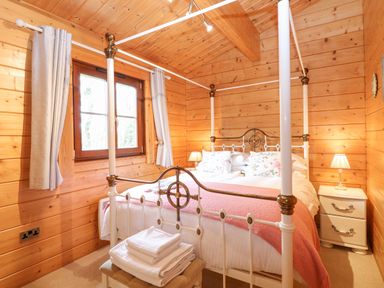 A bedroom with a four poster bed bedside tables and stacked towels at Kingfisher Lodge in Badwell Ash