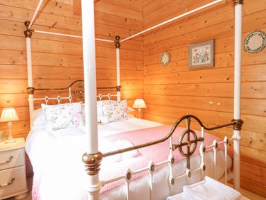 A bedroom with a four poster bed with floral pillows and a pink blanket and wooden walls at Kingfisher Lodge in Badwell Ash