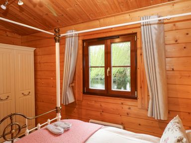 A bedroom with a wooden four-poster bed a wardrobe and a window looking out to trees at Kingfisher Lodge in Badwell Ash